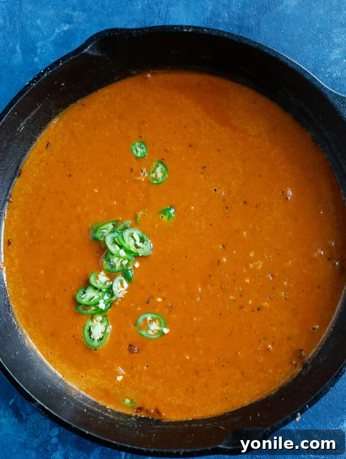 A rich, red curry sauce simmering in a skillet, with onions and spices, waiting for the chicken to be added.