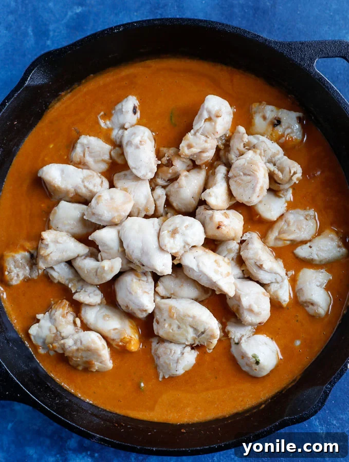 Chicken cubes perfectly coated in the vibrant red curry sauce, simmering gently with fresh cilantro, finishing the cooking process.