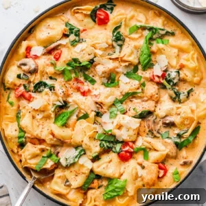 creamy-chicken-tortellini-pasta in a skillet, garnished with basil and shaved parmesan cheese
