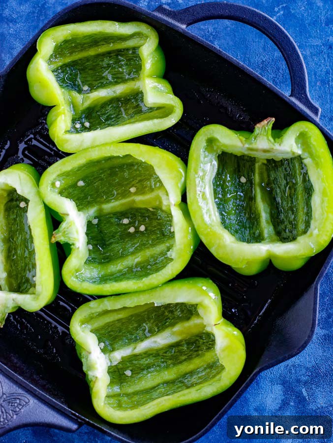 Halved green peppers in a skillet on a blue counter, pre-baking.
