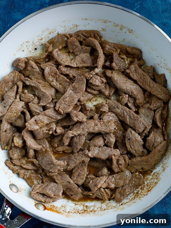 Trimmed steak cooking in a non-stick skillet on a blue counter, searing to perfection.