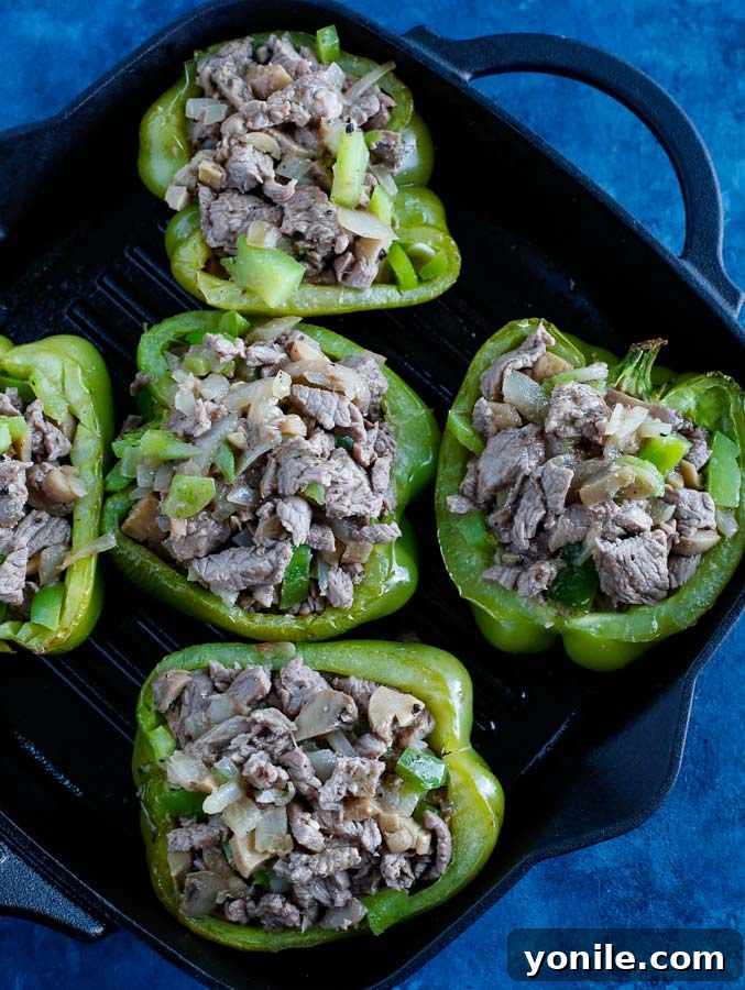 Stuffed bell peppers cooking on a skillet on a blue counter, cheese melting.