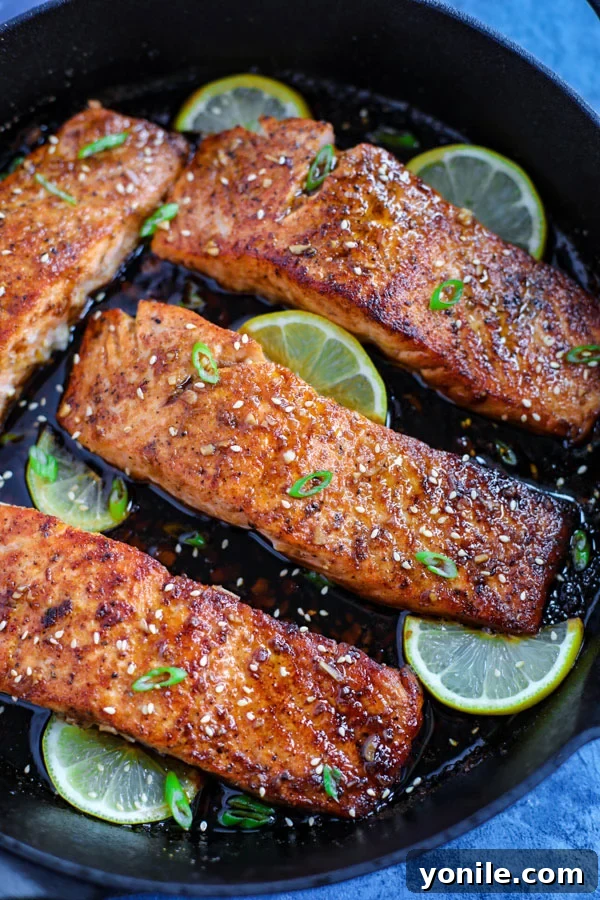 Four spicy honey garlic salmon pieces with lime wedges in a cast ion skillet.