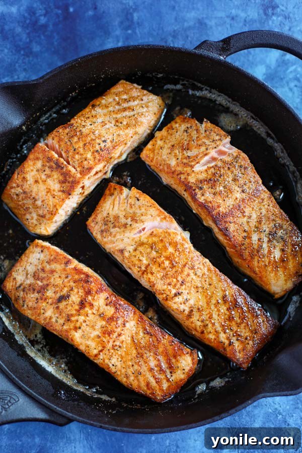 A cast iron skillet with 4 salmon fillets cooking on a blue counter.