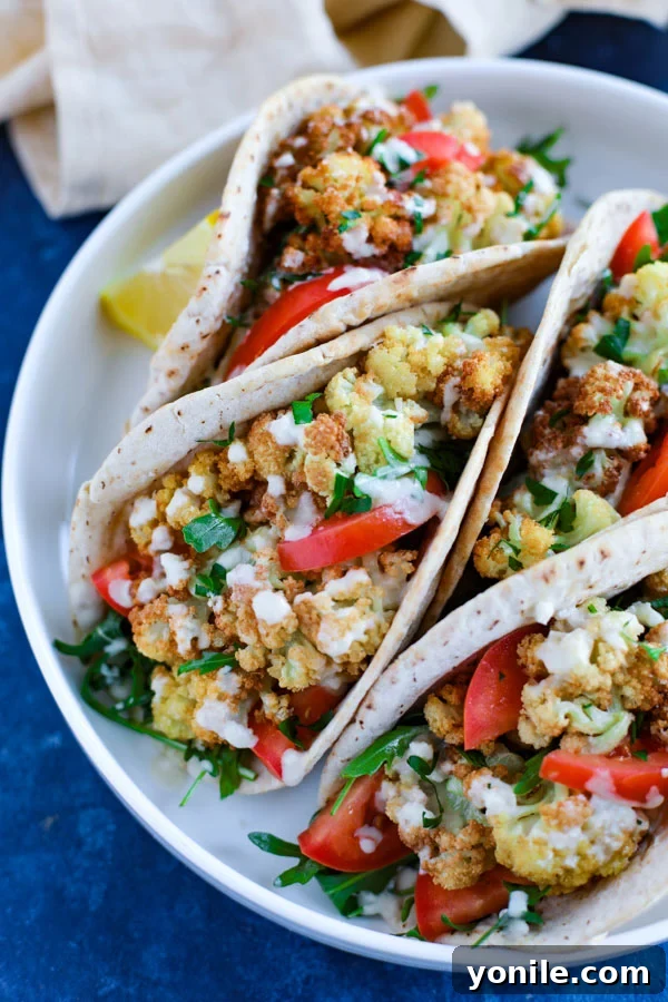 A white plate with four vibrant vegetarian cauliflower pita wraps, garnished with fresh herbs, resting on a rustic blue countertop.
