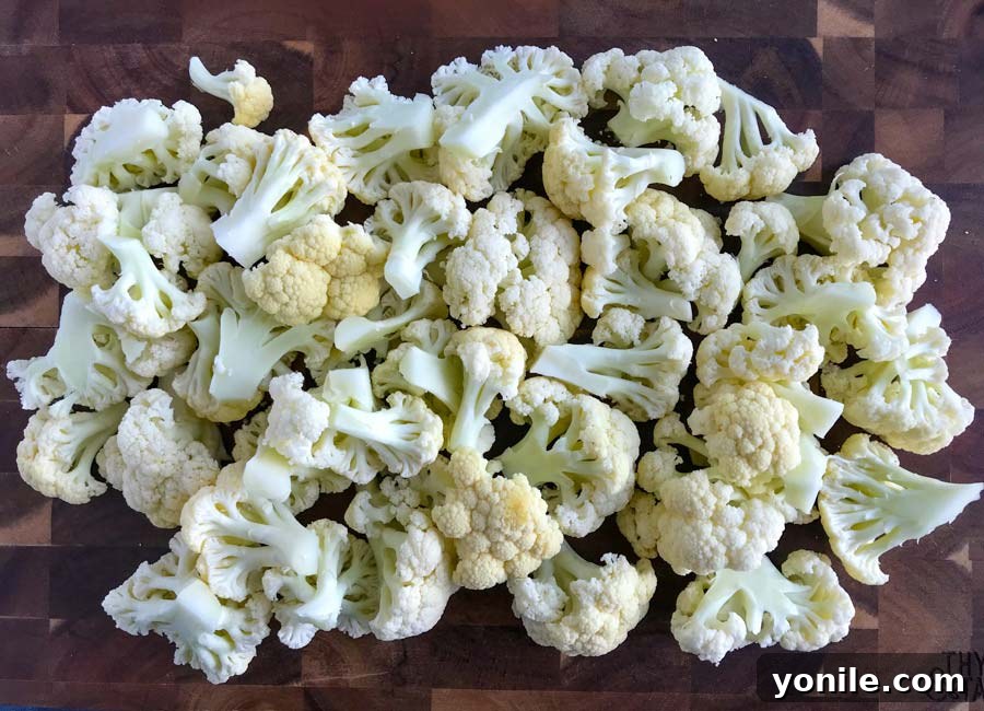 Fresh cauliflower florets, neatly cut and ready for roasting, displayed on a rustic wooden cutting board.