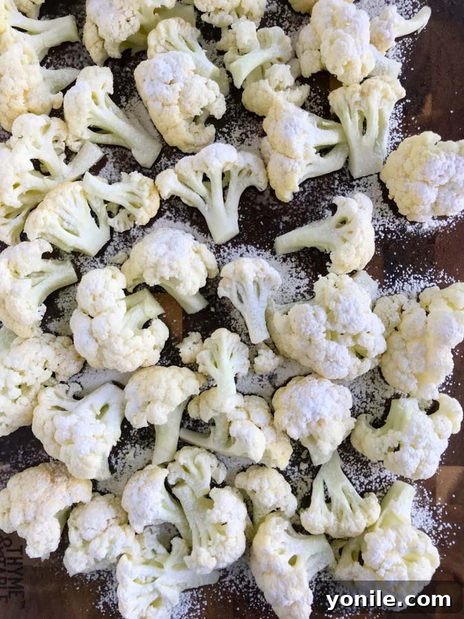 Cauliflower florets, lightly dusted with corn flour, spread evenly on a baking sheet, ready for roasting.