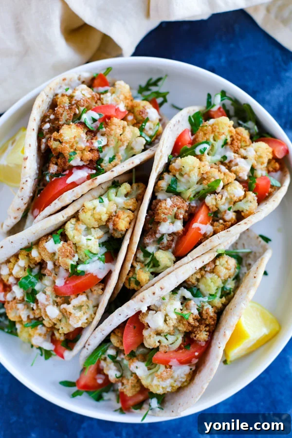 A white plate displaying several vegetarian cauliflower pita wraps, artfully arranged and ready to be enjoyed on a clean blue surface.