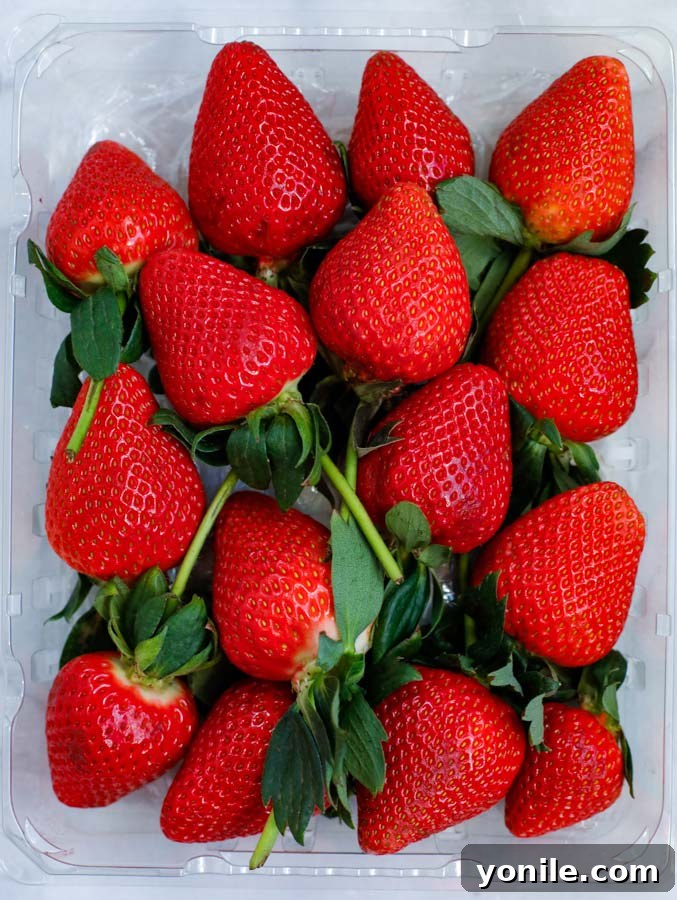 Close-up shot of fresh, vibrant red strawberries nestled in a container, ready to be transformed into a delicious treat.