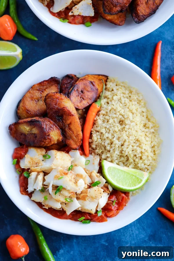 A white bowl with Caribbean Jerk Fish, quinoa, tomato sauce, and fried plantains topped with chilies on a blue counter.