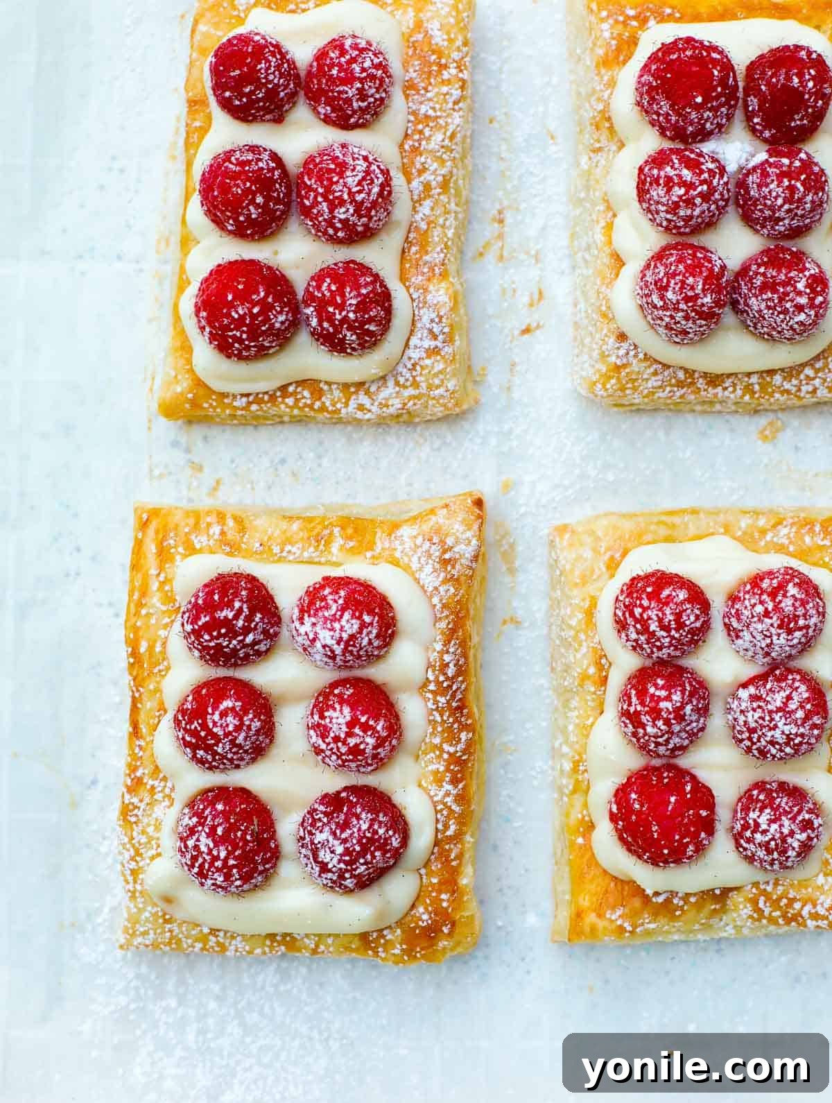 A baking sheet filled with freshly baked raspberry tarts, lightly dusted with powdered sugar, ready to be served.