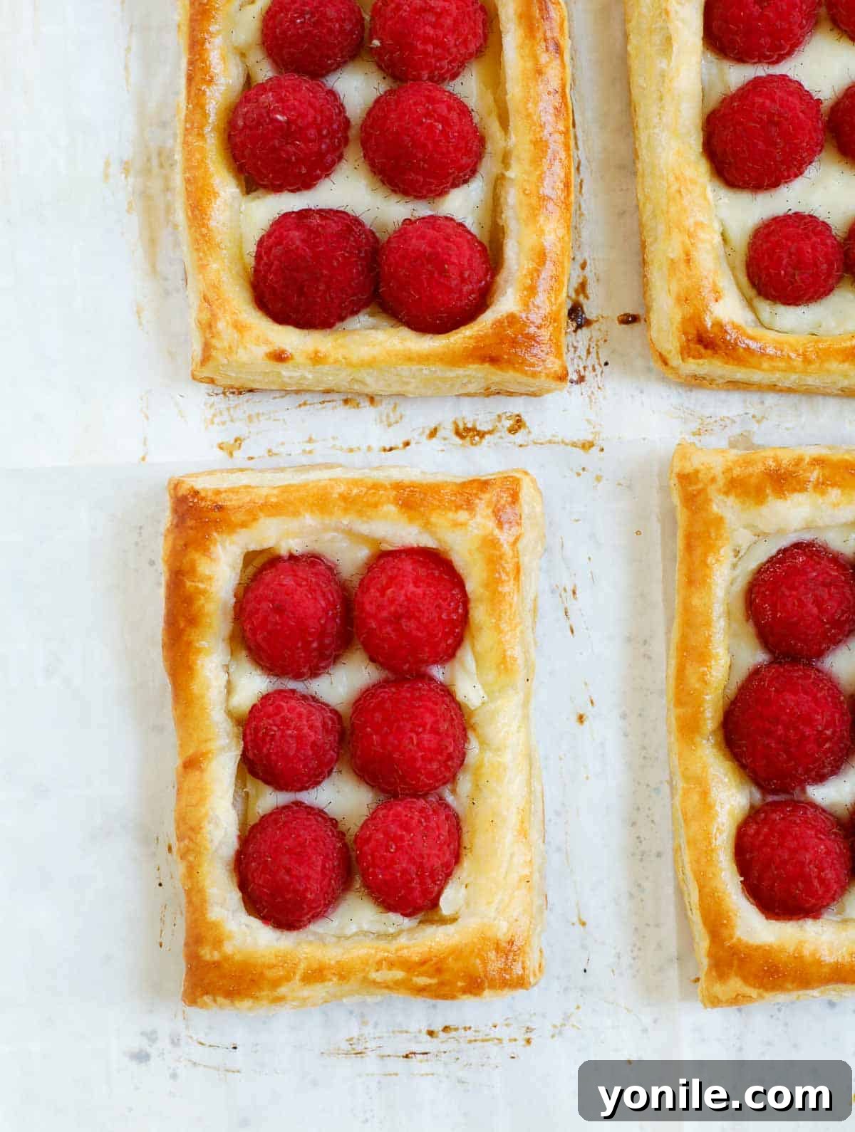Freshly baked raspberry tarts cooling on a sheet pan, with golden-brown pastry and slightly browned raspberries.
