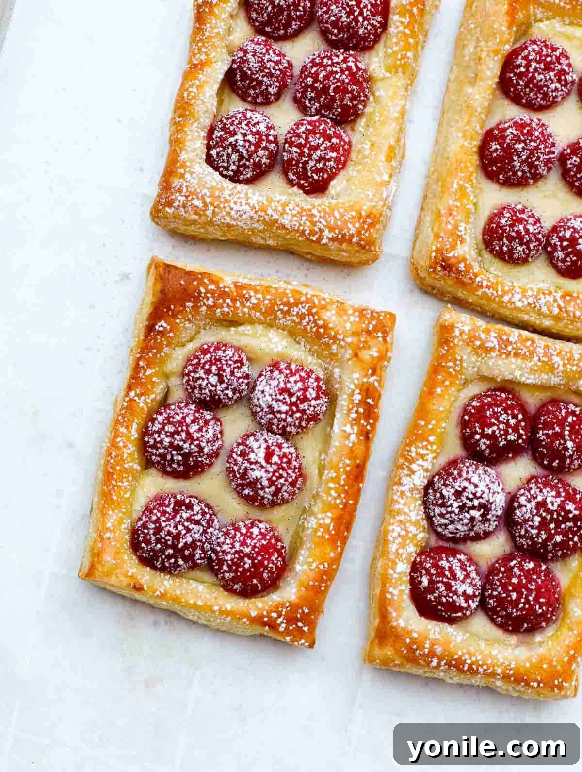 Finished raspberry tarts on a baking sheet, dusted with powdered sugar, showcasing their crisp pastry and vibrant fruit.