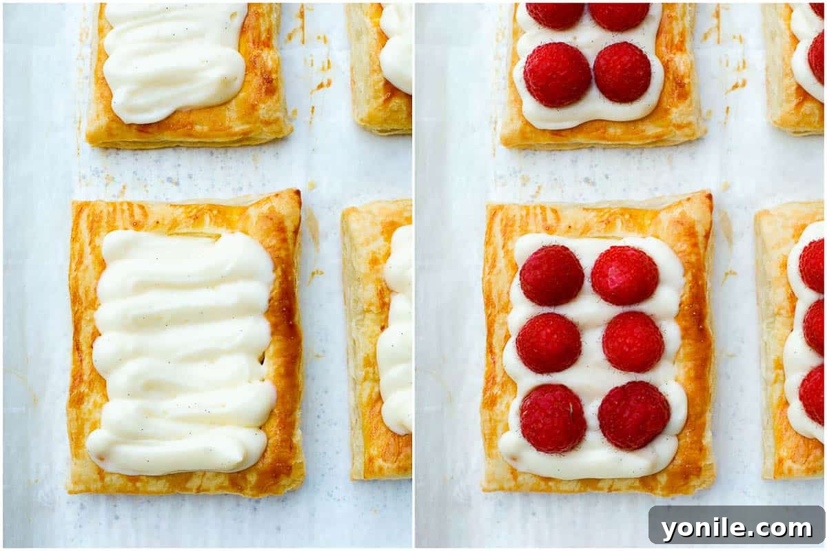 Puff pastry shells filled with piped pastry cream and topped with fresh raspberries, ready to be dusted with sugar.