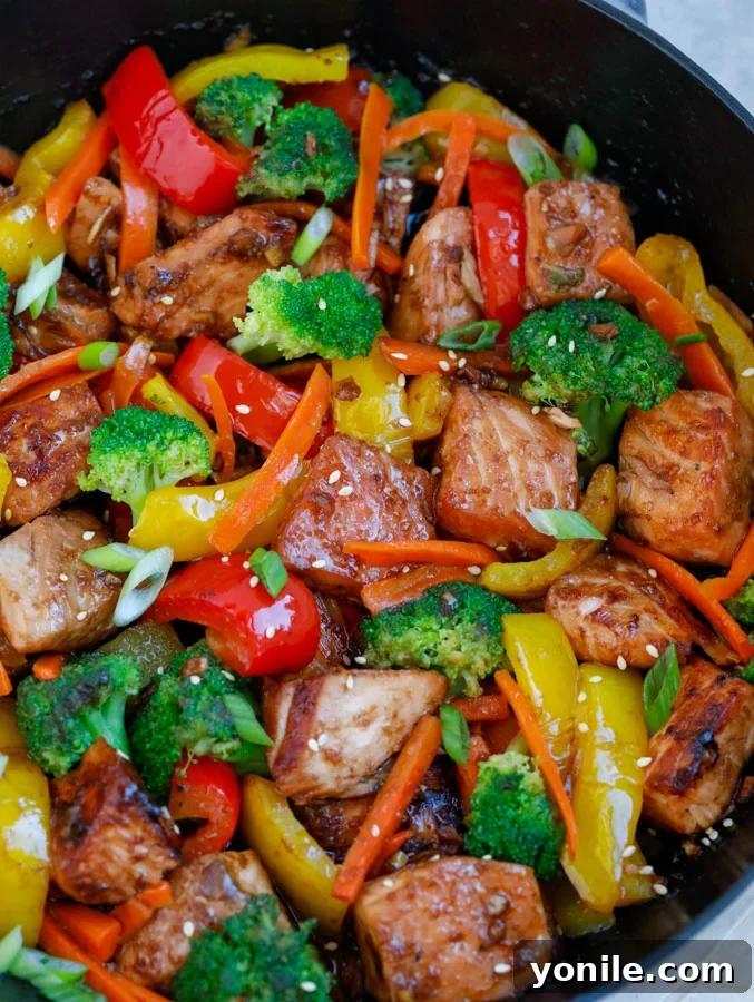 Close-up of Teriyaki Salmon Stir Fry simmering in a large nonstick skillet, showcasing vibrant vegetables and golden-brown salmon pieces.