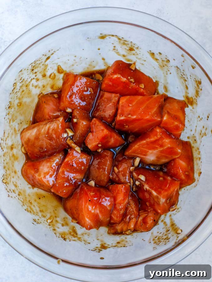 Cubed salmon marinating in a glass bowl with homemade teriyaki sauce, ready for cooking.