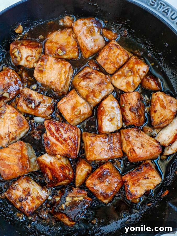 Salmon cubes and teriyaki sauce sizzling in a nonstick skillet, beginning to caramelize.