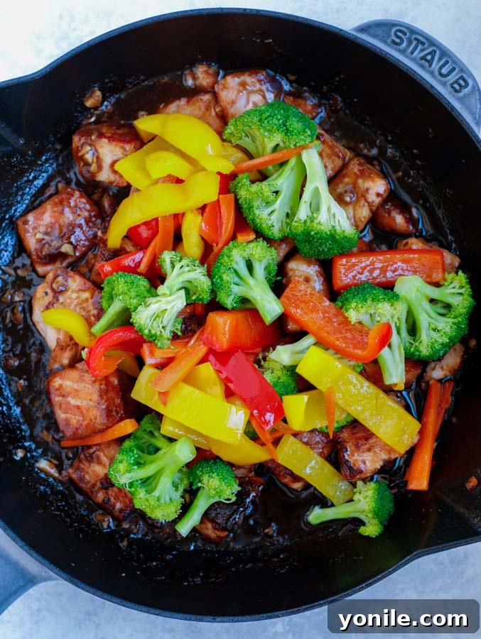 Cooked salmon and stir fry vegetables being gently tossed together in a large nonstick skillet with the remaining teriyaki sauce.