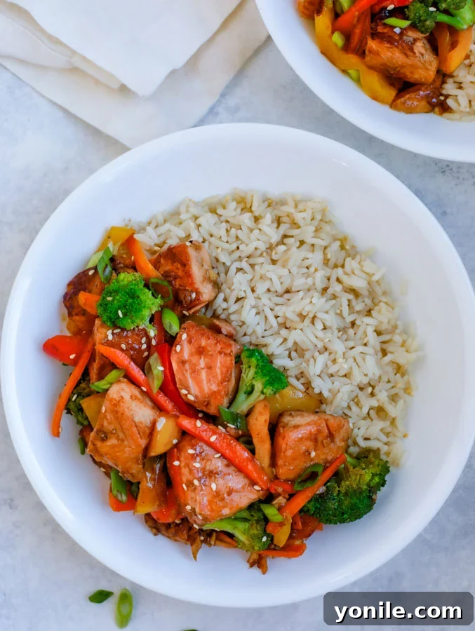 A white bowl filled with Teriyaki Salmon Stir Fry and white rice, placed on a clean white kitchen counter.