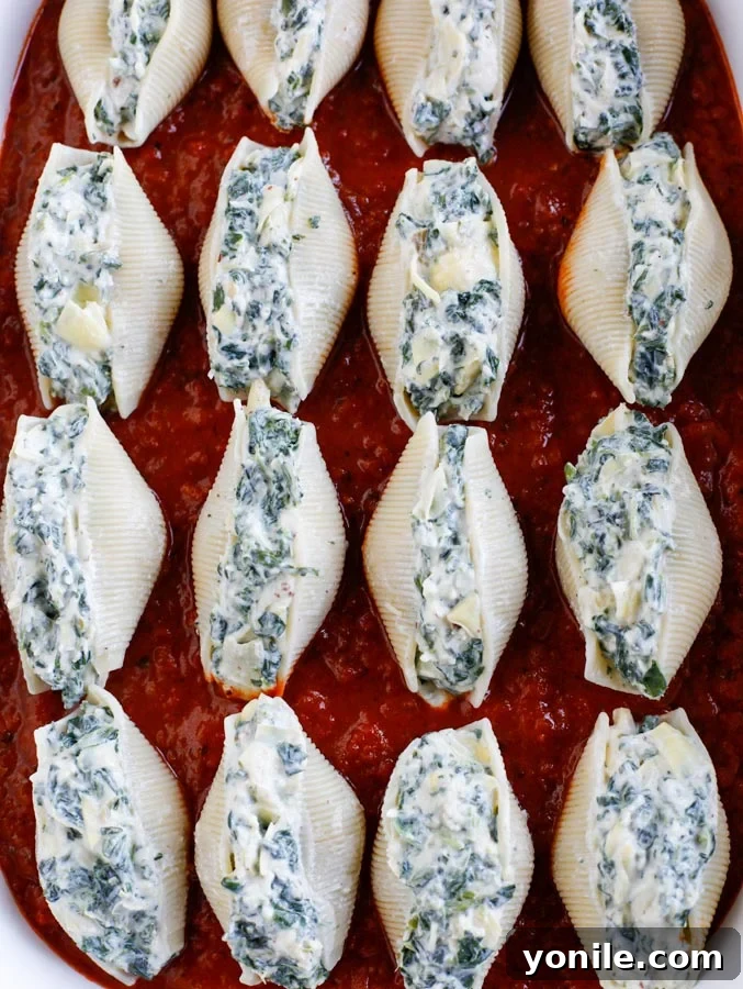 Spinach artichoke stuffed shells lined up in a baking dish.
