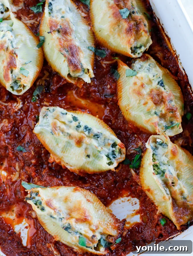 A baking dish with spinach artichoke stuffed shells in tomato basil marinara sauce.
