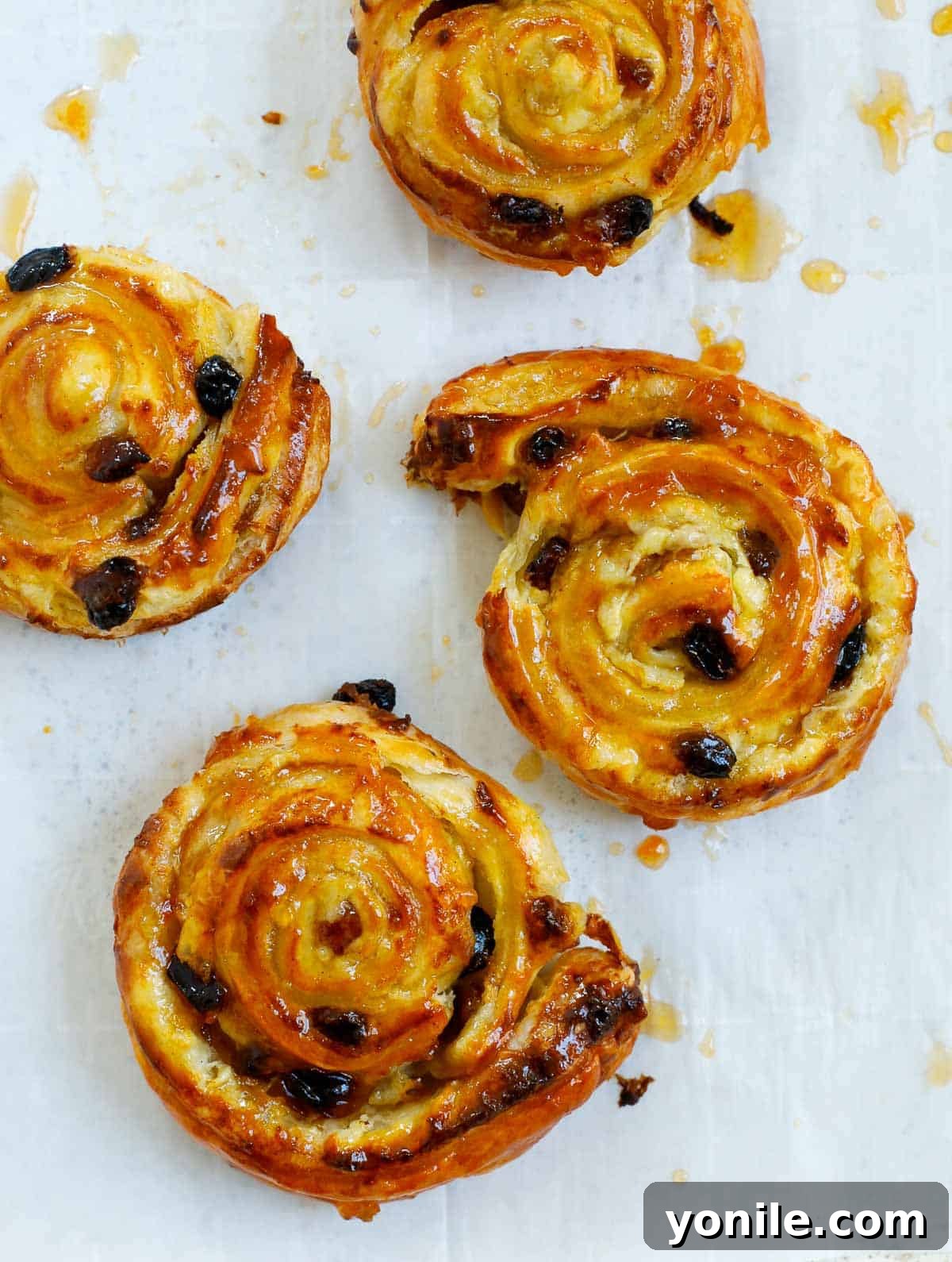 Freshly baked pain aux raisins, puffed and golden, arranged on a parchment-lined baking sheet, just out of the oven.
