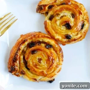 two baked pain aux raisins on a white plate.