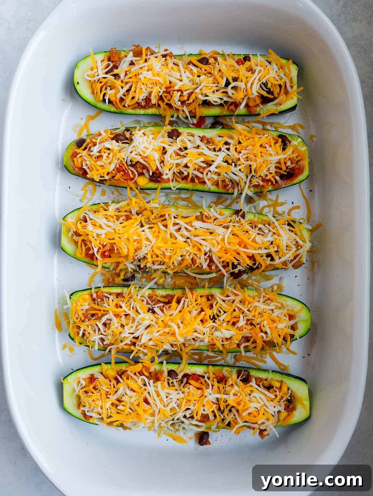 Zucchini boats generously topped with shredded cheese, ready for the final bake