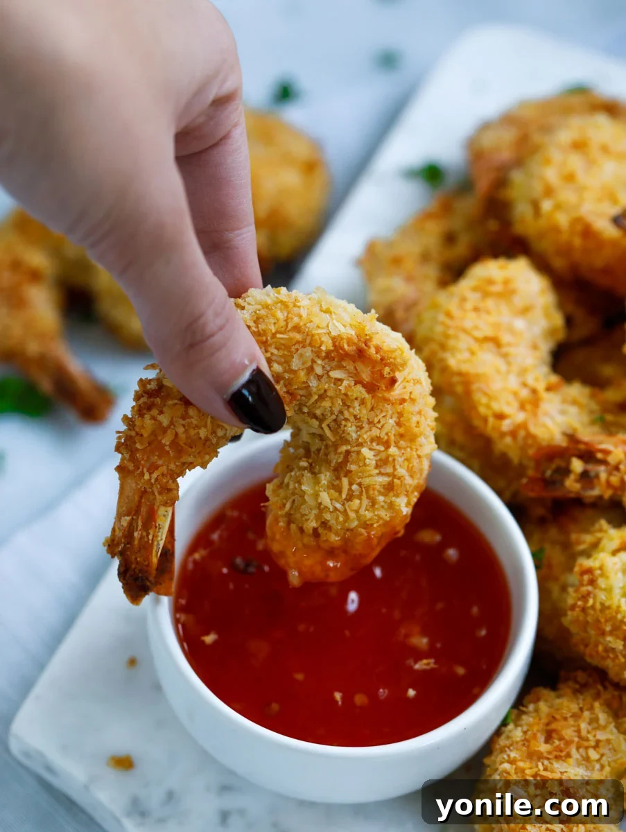 A coconut shrimp being dipped into sweet chili sauce