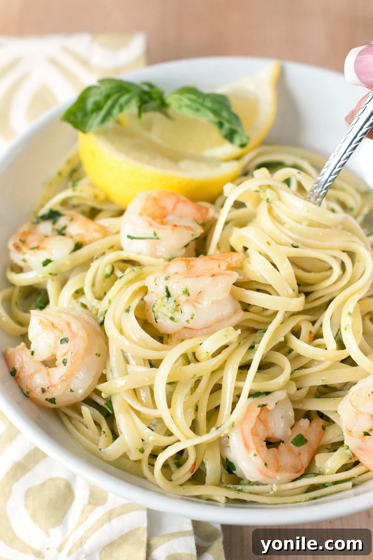 Vibrant Pesto Shrimp Scampi Pasta 4 Overhead picture of a large white bowl of pasta with pesto shrimp scampi, garnished with fresh lemon slices and basil.