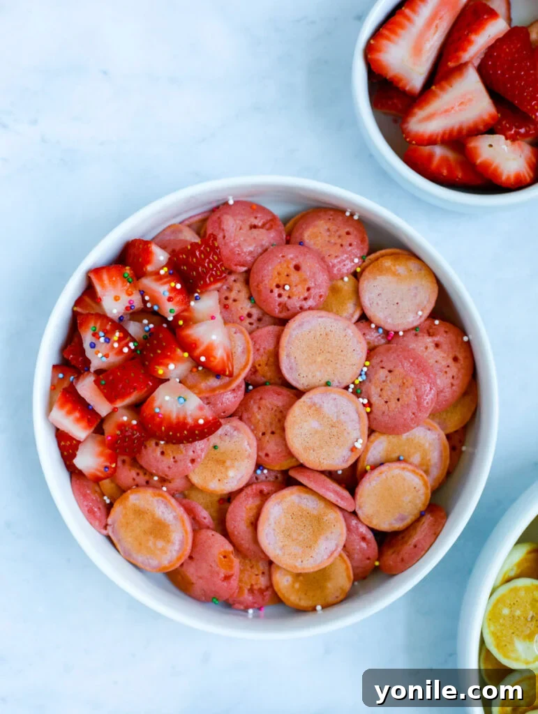 A bowl of mini strawberry pancakes, adorned with fresh strawberries and colorful sprinkles.