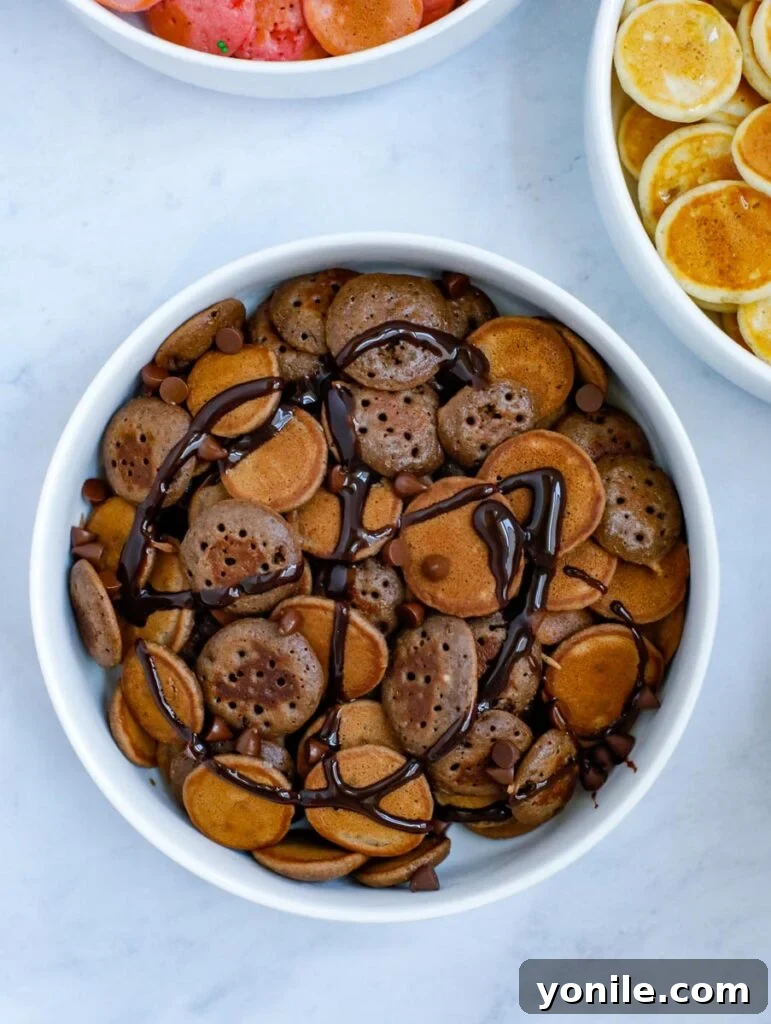 A bowl of mini chocolate pancake cereal, topped with chocolate syrup and chocolate chips.