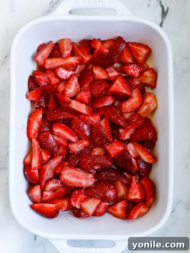 Strawberry crisp filling spread evenly in a buttered baking dish, ready for the topping.