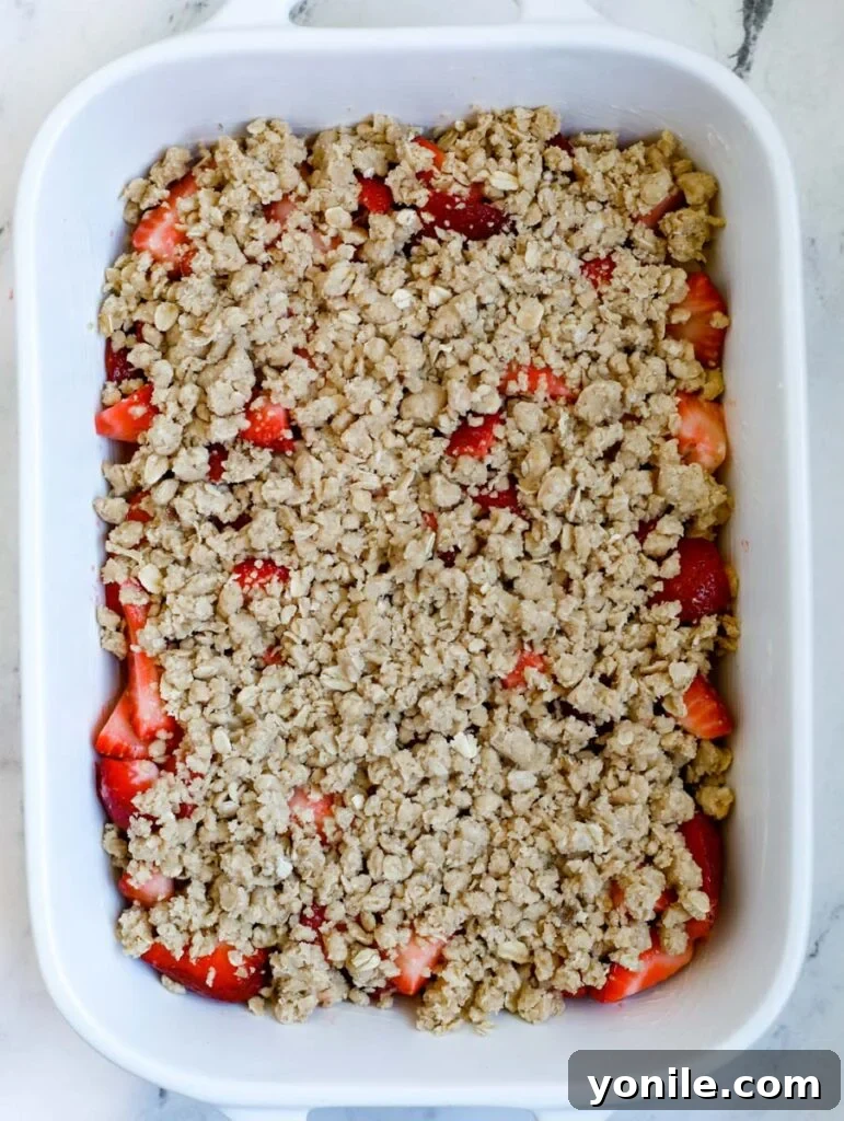 Unbaked strawberry crisp in a baking dish, with the golden crumb topping spread over the vibrant strawberries.