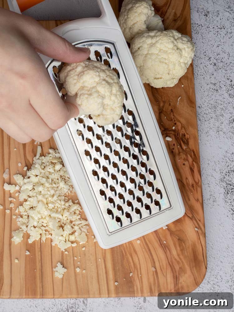 Close-up of a person grating cauliflower using a box grater