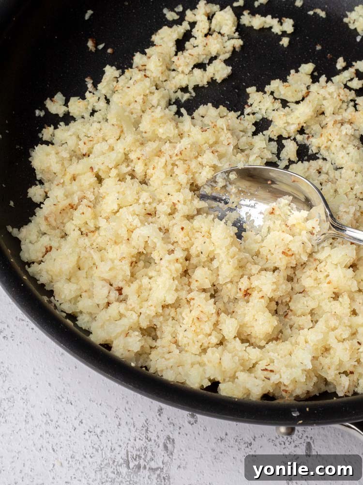 Cauliflower rice being cooked in a skillet on a stovetop