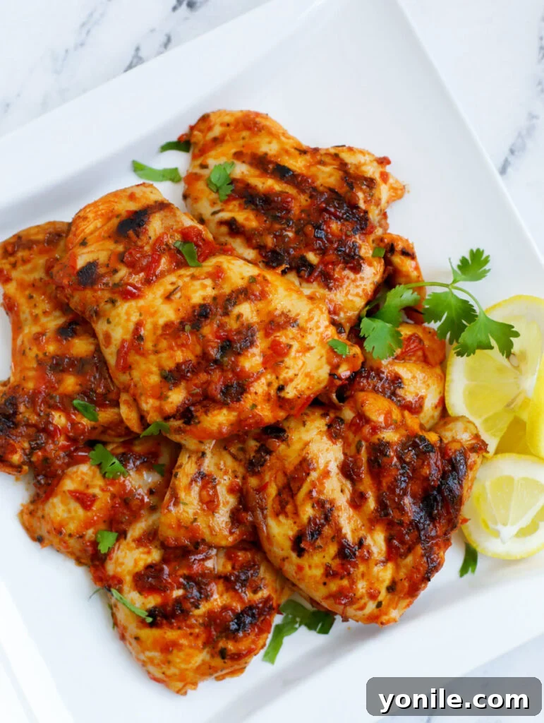 Harissa-Infused Grilled Chicken Thighs 7 Overhead shot of grilled Harissa Chicken on a platter with fresh herbs and lemon, indicating a satisfying meal.