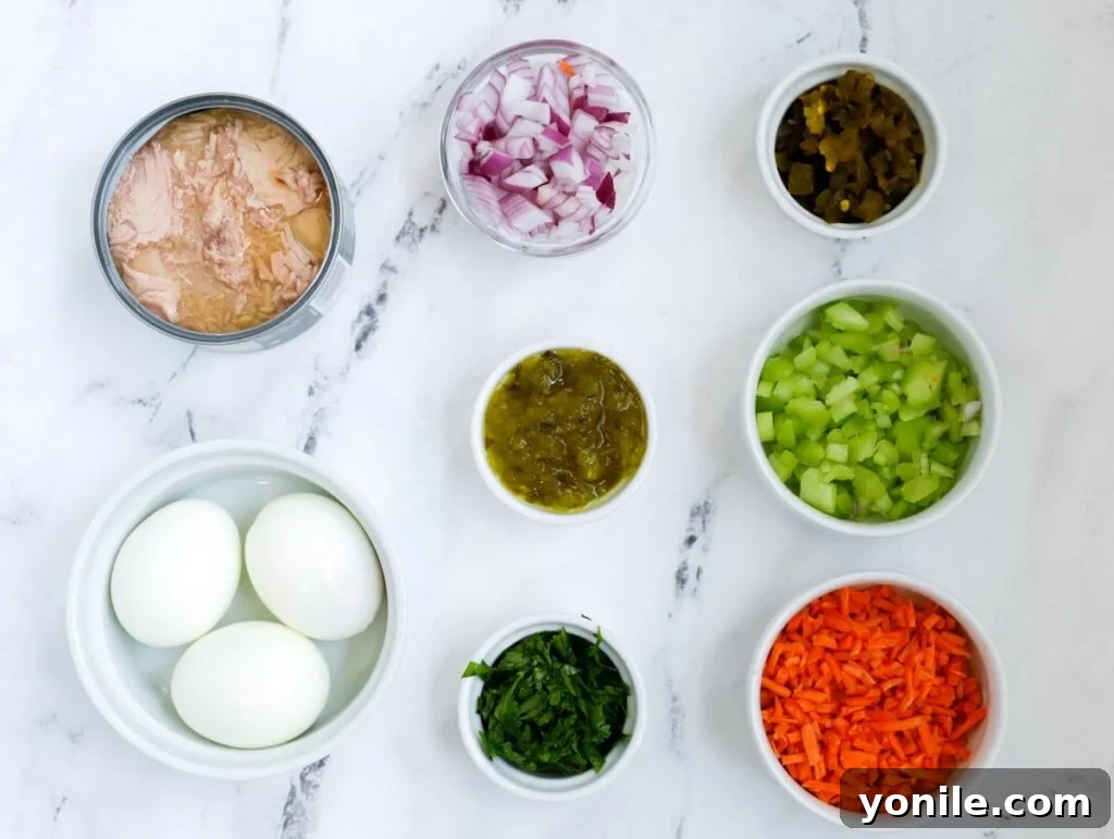 A colorful array of fresh ingredients laid out for Tuna Pasta Salad preparation, including rotini, tuna, and various chopped vegetables.