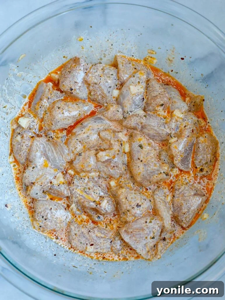 Cubed chicken tenders marinating in a flavorful sauce, ready to be combined with vegetables.