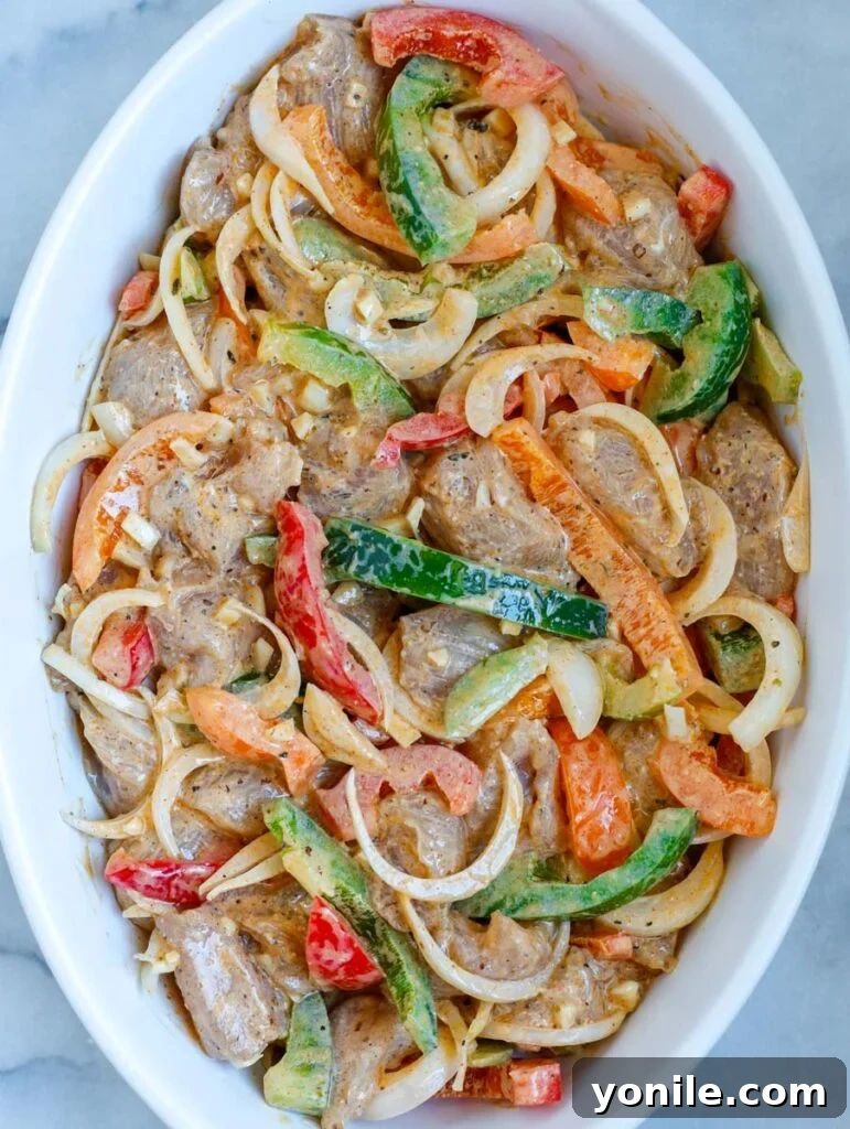 Chicken and colorful fajita vegetables coated in marinade, spread evenly in a baking dish before oven.