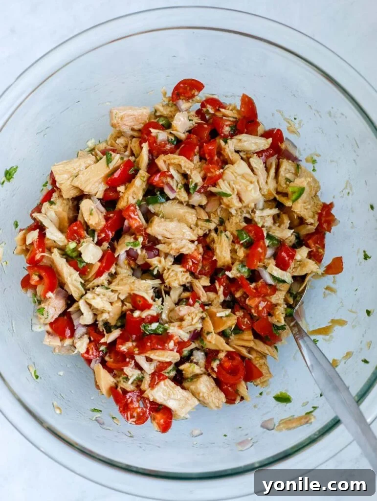 A close-up shot of the Tuna Ceviche mixture, showing tuna chunks combined with diced tomatoes, onions, and green herbs, being tossed in a bowl.