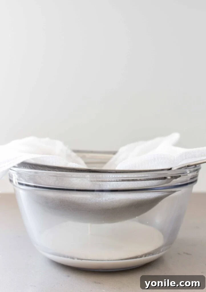 straining almond milk through a cheesecloth and strainer into a bowl