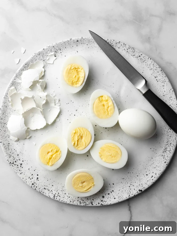Peeled hard-boiled eggs on a plate with some slices showing the creamy yolks.