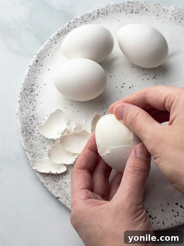 A hand gently peeling the shell off a hard-boiled egg under running water.