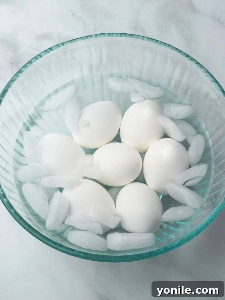 Mastering the Soft Boiled Egg 6 Cooked eggs submerged in a bowl of ice water, crucial for stopping the cooking process and aiding in peeling.