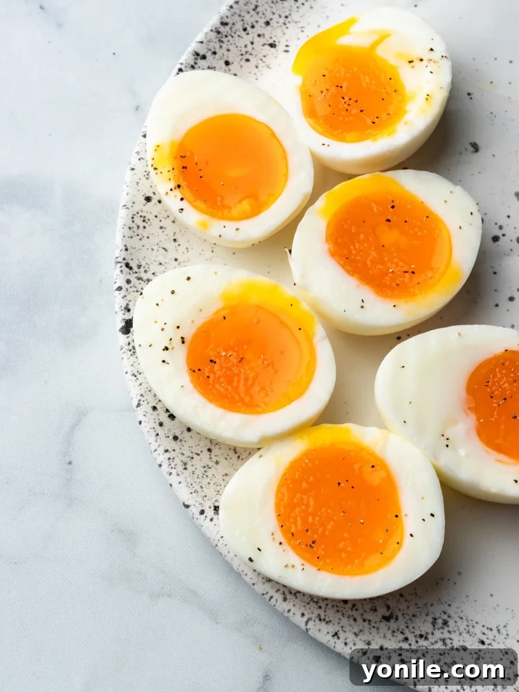 Mastering the Soft Boiled Egg 7 Close-up of perfectly cooked soft-boiled eggs, sliced in half, with vibrant runny yolks on a simple white plate.