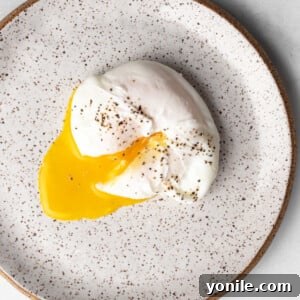 A perfectly poached egg on a plate, with the creamy yolk cut through and seasoned with black pepper.