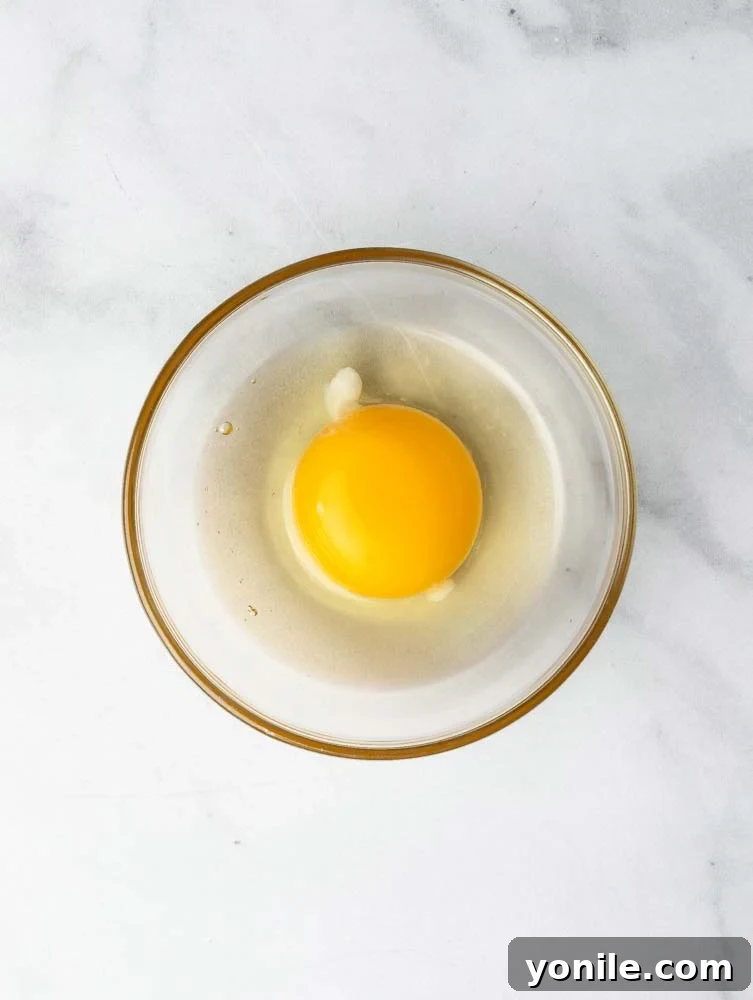 Mastering the Poached Egg 3 A cracked egg carefully placed in a small bowl, showcasing its intact yolk and whites, ready for poaching.