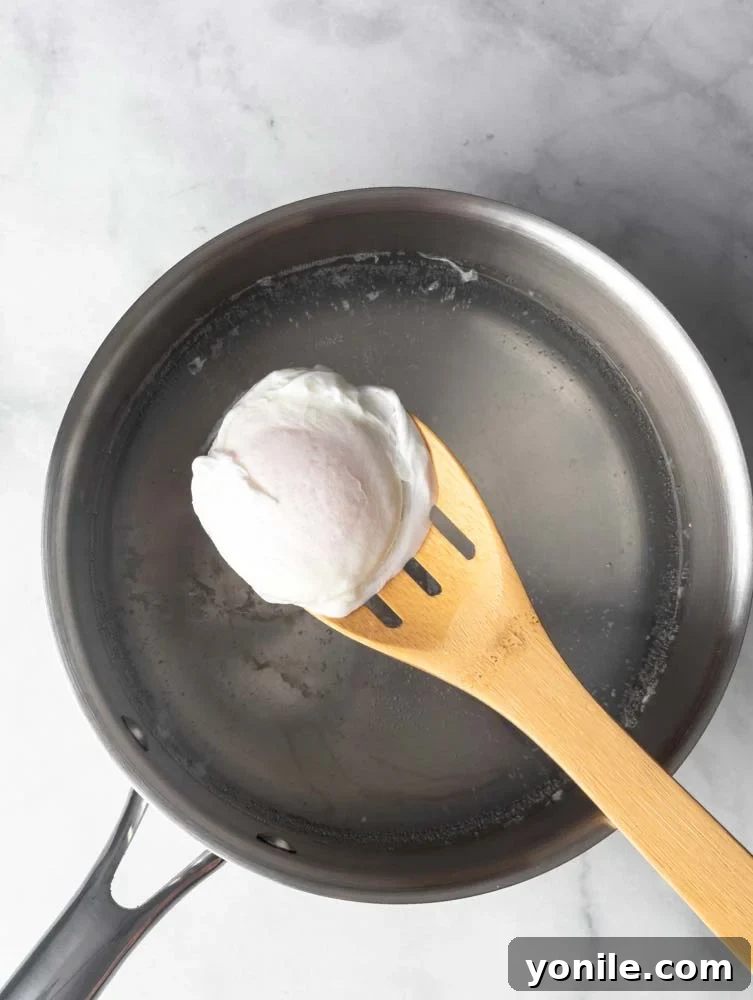 Mastering the Poached Egg 8 A freshly poached egg resting on a wooden slotted spoon, showing its firm whites and delicate shape.