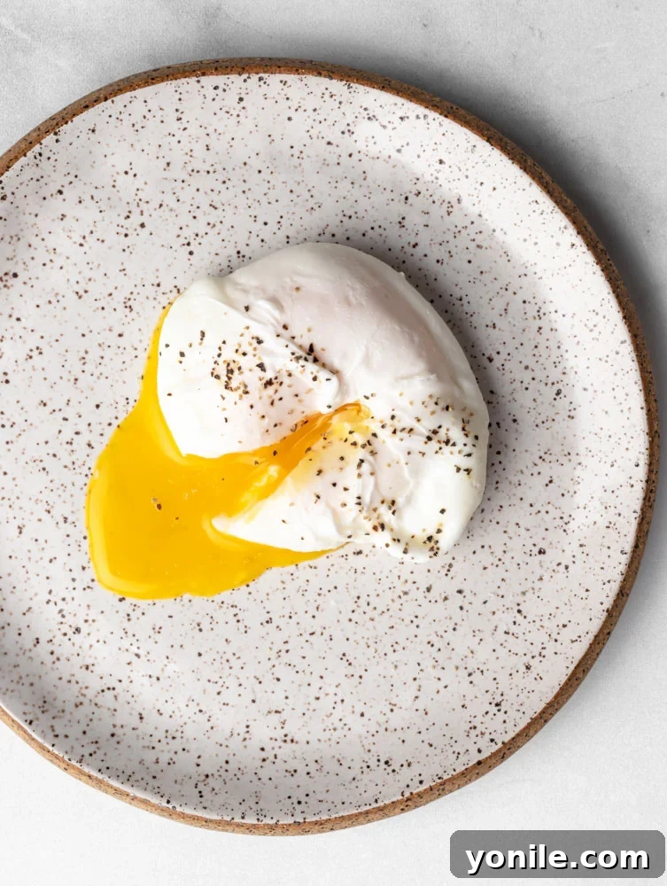 Mastering the Poached Egg 10 A close-up of a perfectly poached egg on a plate, with the yolk gently cut to show its runny texture, seasoned generously with black pepper.